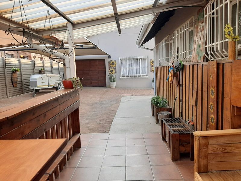 A covered patio area featuring tiled flooring and a polycarbonate roof, overlooking a paved driveway and garage entrance.