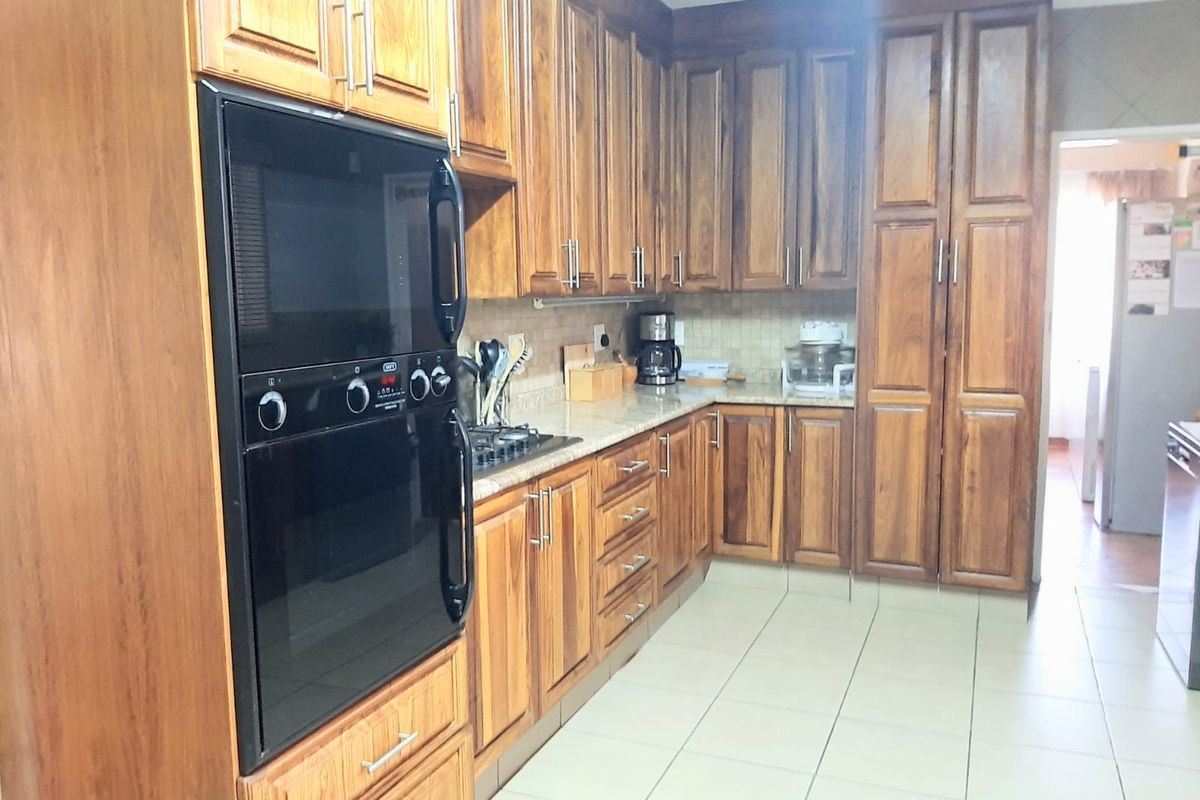 A functional kitchen featuring warm-toned wooden cabinetry, granite countertops, a built-in oven, and a gas hob with tiled flooring and backsplash.