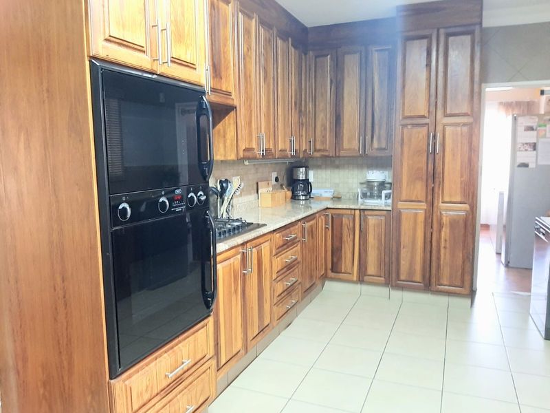 A functional kitchen featuring warm-toned wooden cabinetry, granite countertops, a built-in oven, and a gas hob with tiled flooring and backsplash.