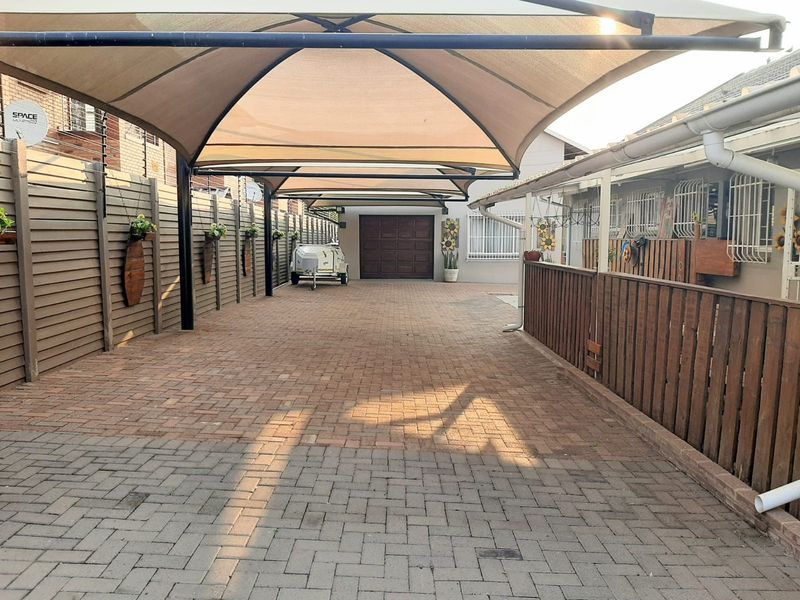 A well-maintained paved driveway featuring a large shade sail carport and secure perimeter fencing leading to a private garage.