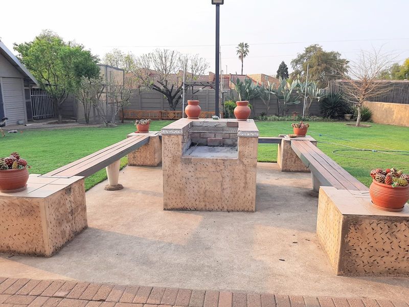Outdoor entertainment area featuring a central built-in braai with integrated concrete bench seating, set within a spacious garden.