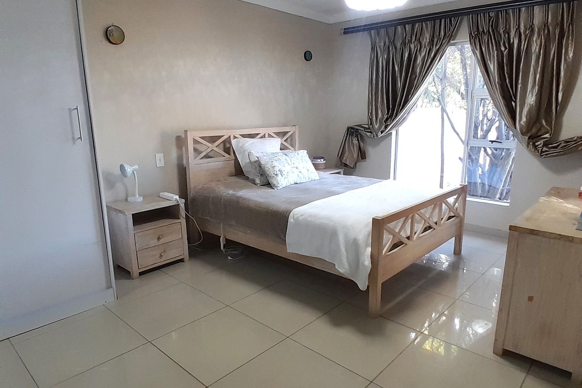 A bedroom featuring tiled flooring, a built-in wardrobe, and a ceiling fan with light, offering a functional and neutral living space.