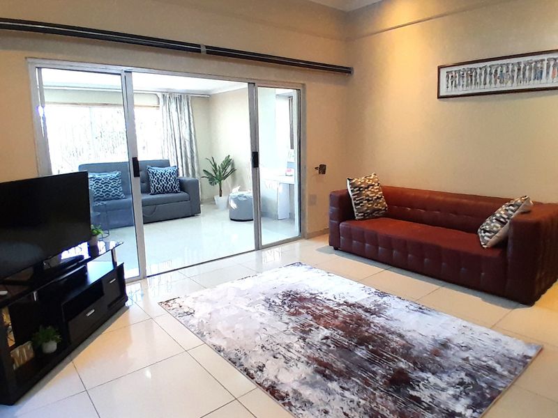 A bright living room featuring large sliding glass doors that open onto an adjacent patio area, finished with neutral floor tiles.