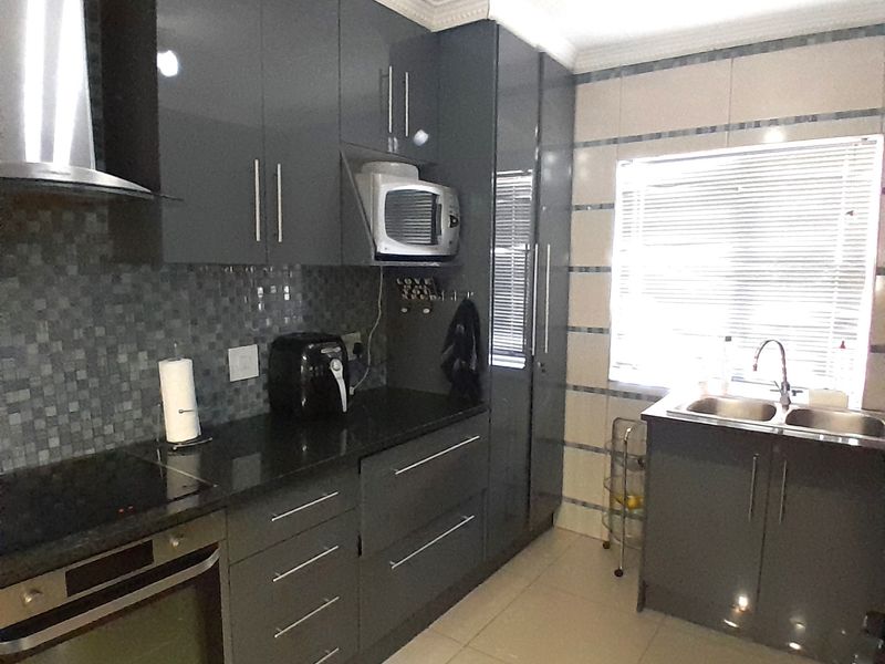 Modern kitchen featuring high-gloss grey cabinetry, granite countertops, built-in oven, extractor fan, and a double basin sink with tiled backsplash.