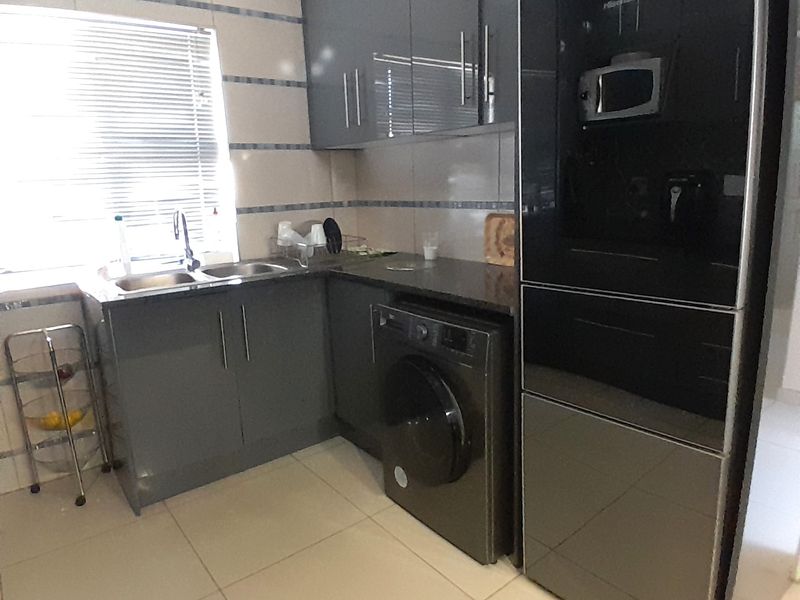 Modern kitchen featuring dark grey cabinetry, tiled splashbacks, double sink, and integrated laundry appliance space with neutral floor tiles.