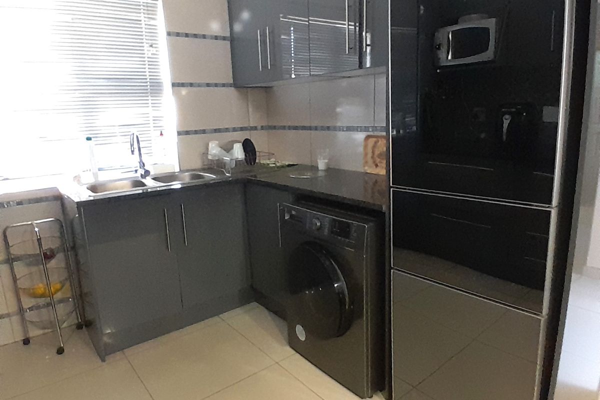 Modern kitchen featuring dark grey cabinetry, tiled splashbacks, double sink, and integrated laundry appliance space with neutral floor tiles.
