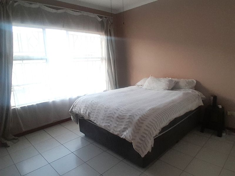 A bedroom featuring tiled flooring, a ceiling fan, and security bars on the window, providing a functional living space.