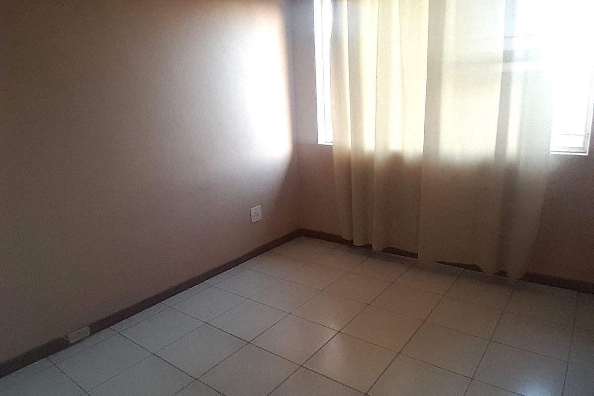An empty bedroom featuring neutral wall paint, tiled flooring, and a window with installed curtain tracks.