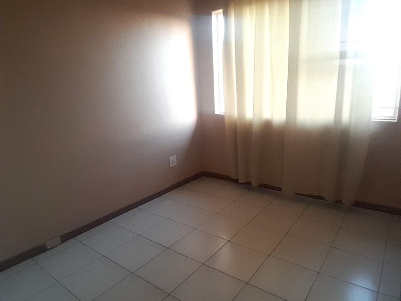 An empty bedroom featuring neutral wall paint, tiled flooring, and a window with installed curtain tracks.