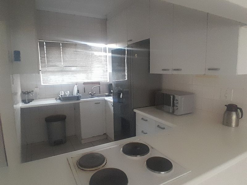 A functional kitchen featuring white cabinetry, a built-in electric hob, and a stainless steel sink with a window providing natural light.