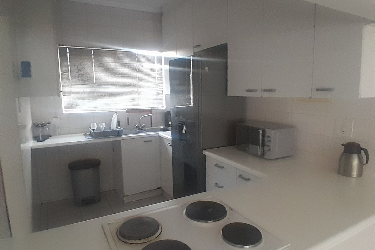 A functional kitchen featuring white cabinetry, a built-in electric hob, and a stainless steel sink with a window providing natural light.