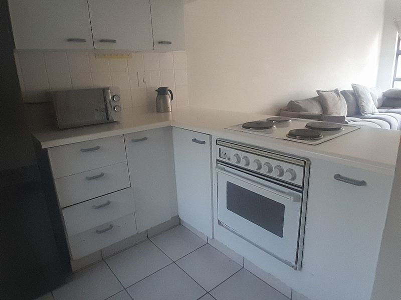 Open-plan kitchen featuring white cabinetry, tiled flooring, and a built-in electric oven and hob, seamlessly connecting to the adjacent living area.