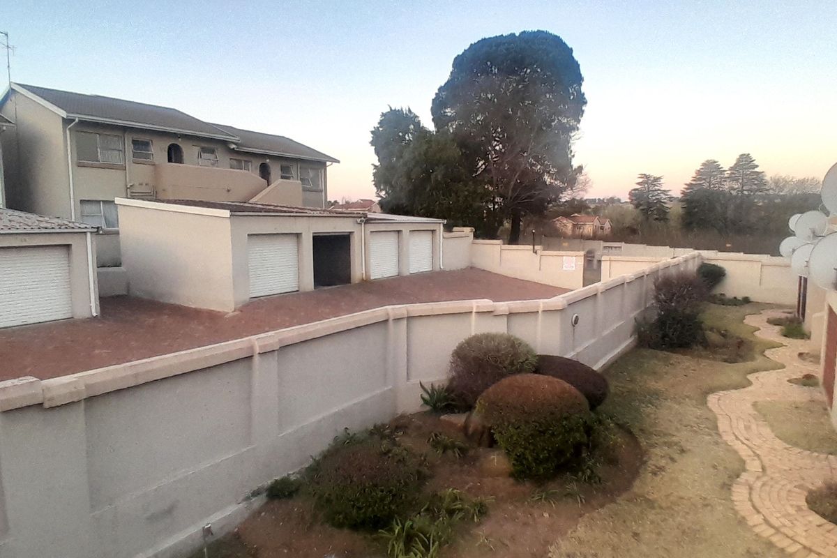 An elevated view of the rear exterior area featuring a paved driveway, multiple garage units, a perimeter wall, and a landscaped garden with a brick pathway.