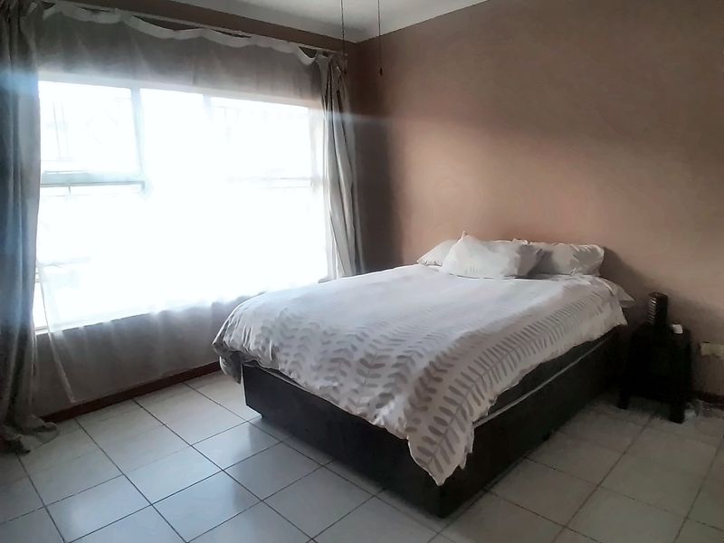 A bedroom featuring tiled flooring and a ceiling fan, with natural light entering through a large window.