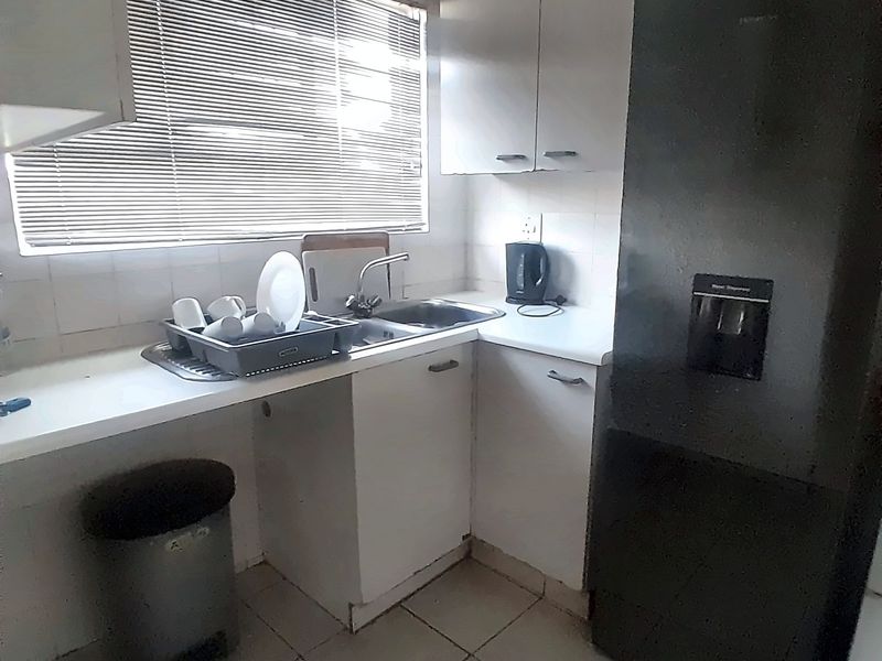 A compact kitchen featuring built-in cabinetry, a stainless steel sink, and tiled flooring, offering a functional space in need of cosmetic updates.