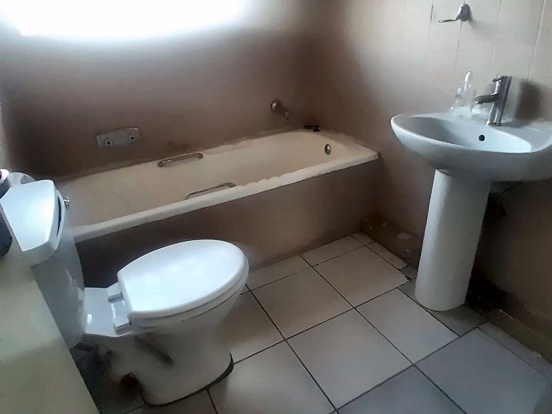 A functional bathroom featuring a pedestal basin, bathtub, and toilet with tiled finishes, offering a blank canvas for potential modernization and renovation.
