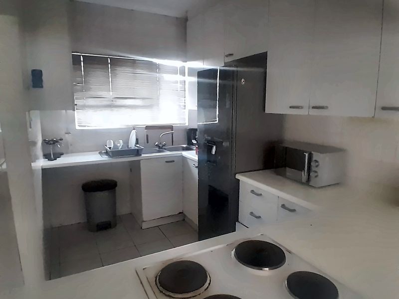 A compact kitchen featuring white built-in cabinetry, an electric hob, and a stainless steel sink, requiring cosmetic updates to modernize the space.