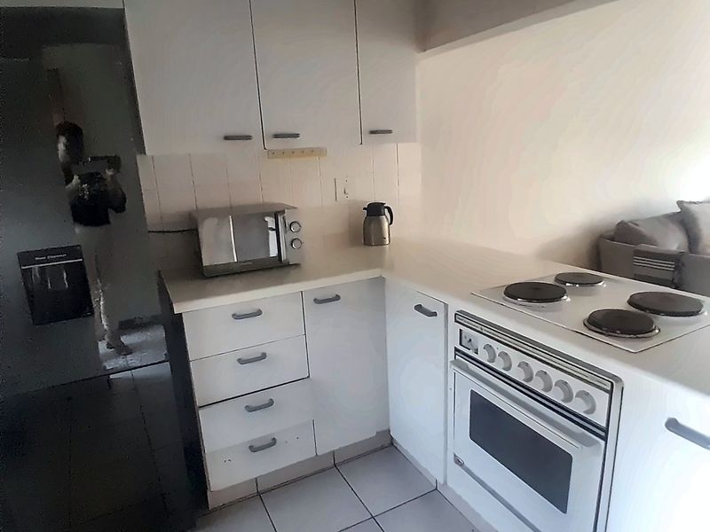 A compact kitchen featuring white cabinetry, a built-in oven with an electric hob, and tiled flooring.