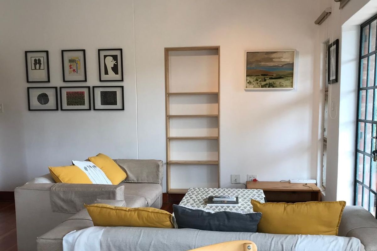 A bright living room featuring timber flooring, built-in shelving, and a large steel-framed glass door providing natural light.