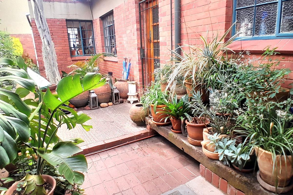 A rear courtyard area featuring exposed brick walls, steel-framed windows, and a paved patio with a raised brick planter.