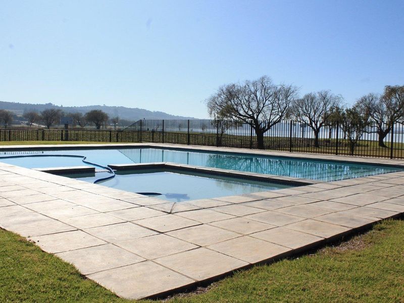 A well-maintained outdoor swimming pool area featuring paved surrounds and metal perimeter fencing with scenic landscape views.