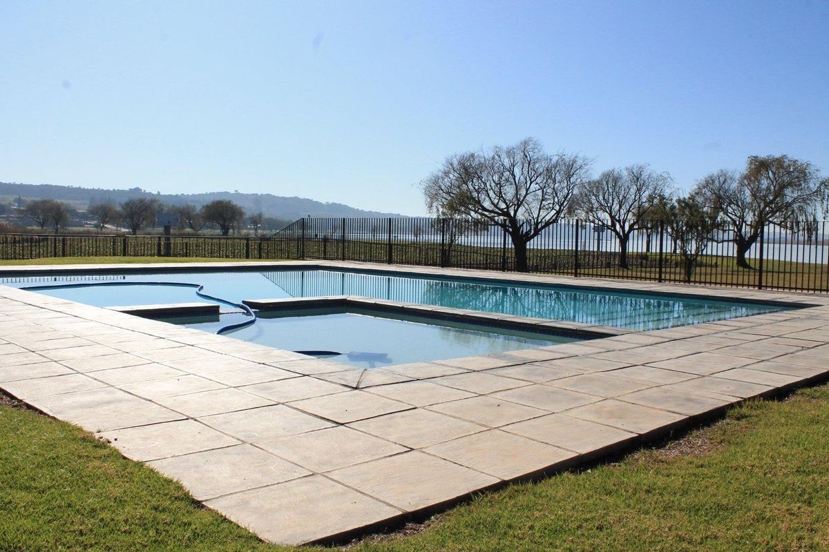 A well-maintained outdoor swimming pool area featuring paved surrounds and metal perimeter fencing with scenic landscape views.
