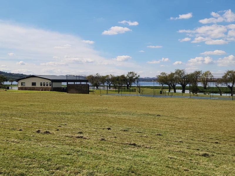 Expansive residential land featuring a sports facility, stone-clad building, and scenic water views in a peaceful, open setting.