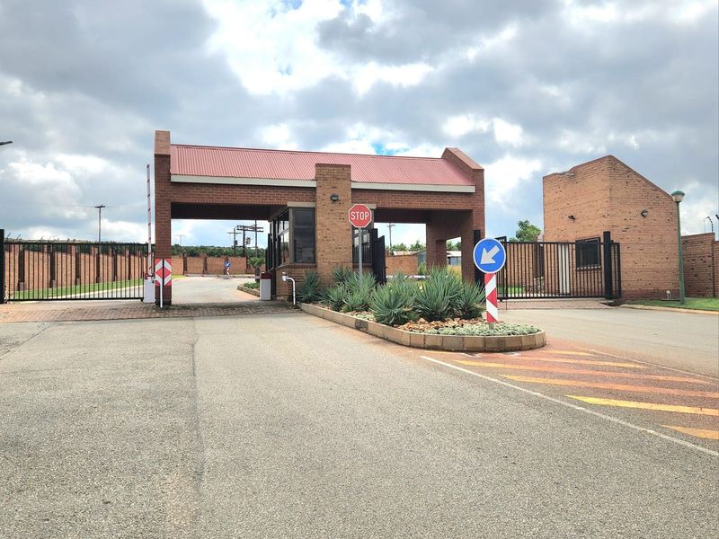 A secure residential estate entrance featuring a brick gatehouse, automated boom gates, and paved driveway access.