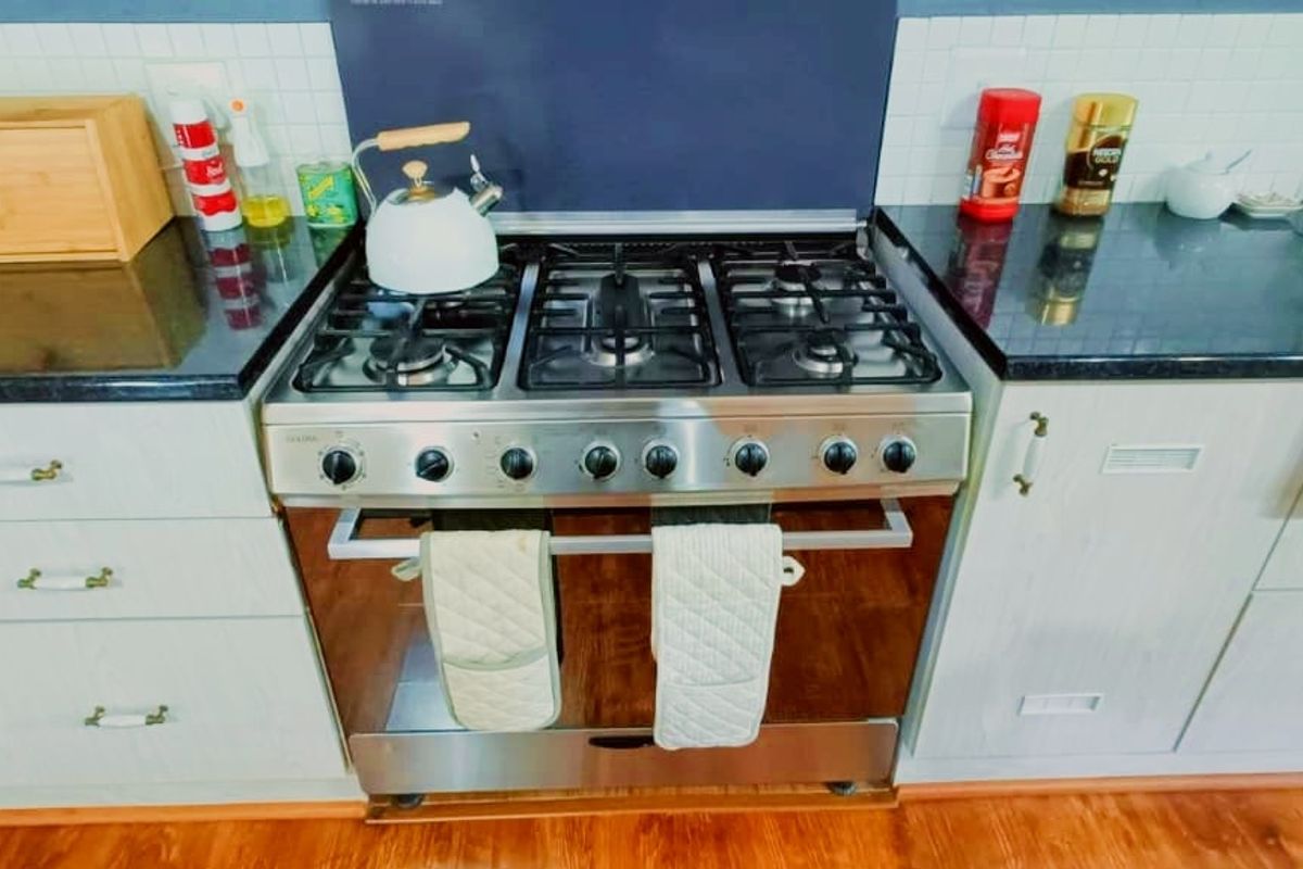 A functional kitchen area featuring a stainless steel gas stove and oven, dark granite countertops, and light-toned cabinetry with a tiled backsplash.