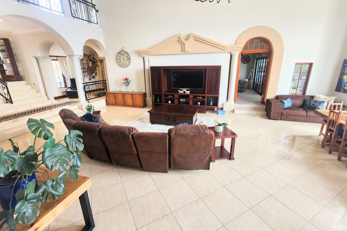 Spacious open-plan living area featuring high ceilings, tiled floors, arched architectural details, and a mezzanine level with wrought iron railings.