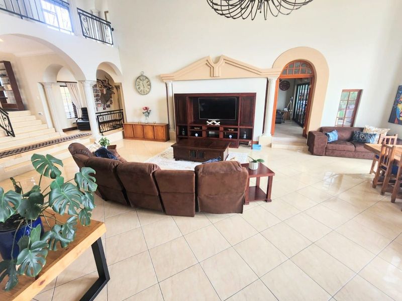 Spacious open-plan living area featuring high ceilings, tiled floors, arched architectural details, and a mezzanine level with wrought iron railings.