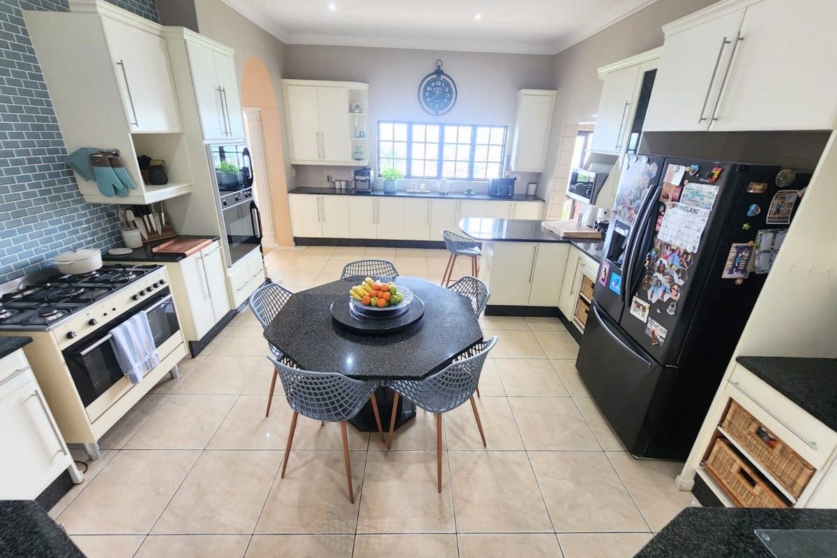 Spacious kitchen featuring granite countertops, gas hob, built-in oven, and ample cabinetry with a tiled splashback and neutral floor tiles.
