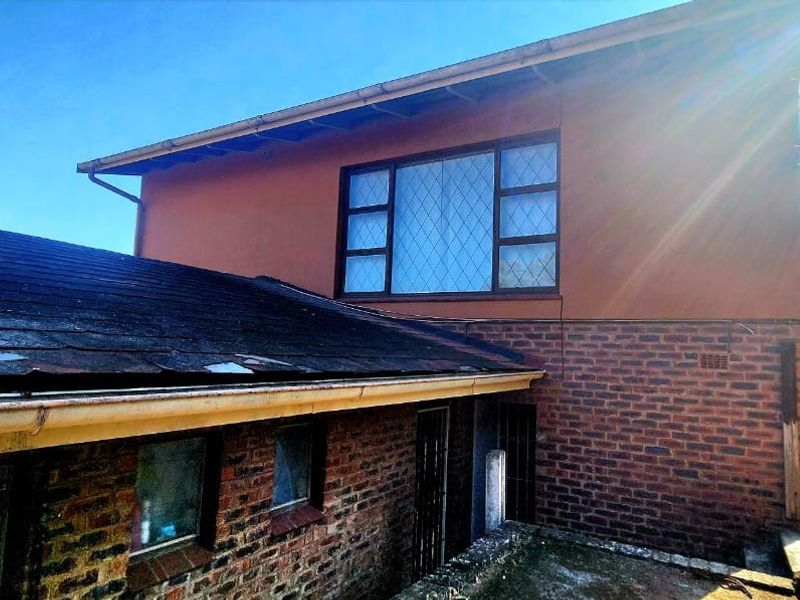 Rear exterior view of the property showing brick facade, leaded glass windows, and a tiled roof requiring maintenance and repair.