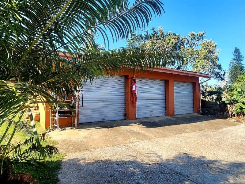 A triple garage with roller doors and a concrete driveway, situated in a garden setting.