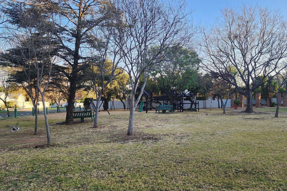 A spacious, well-established garden area featuring mature trees, perimeter fencing, and a dedicated playground structure for outdoor recreation.