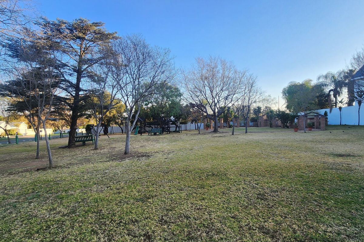 A spacious, well-maintained garden area featuring mature trees, expansive lawn, and perimeter fencing, providing a peaceful outdoor setting.