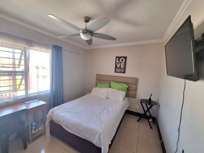 A functional bedroom featuring tiled flooring, a ceiling fan, and a window allowing natural light.