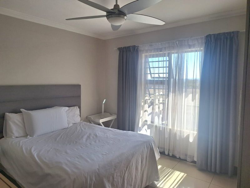 A well-lit bedroom featuring tiled flooring, a ceiling fan, and large windows with security bars, offering a comfortable and functional living space.