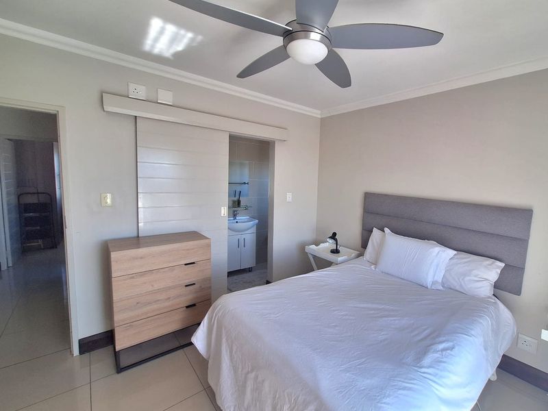 A well-maintained bedroom featuring tiled flooring, a modern ceiling fan, and direct access to an en-suite bathroom via a sliding door.