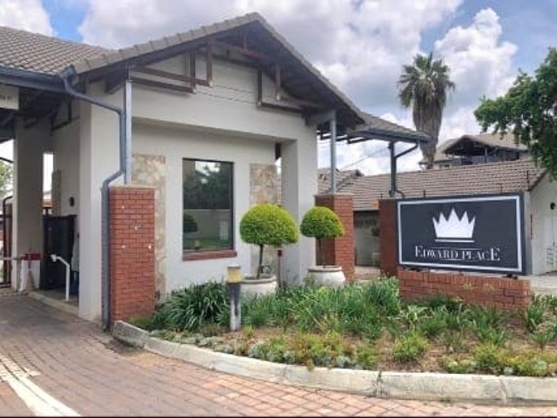 The entrance to Edward Place apartment complex, featuring a brick-accented security gatehouse, paved driveway, and landscaped garden area.