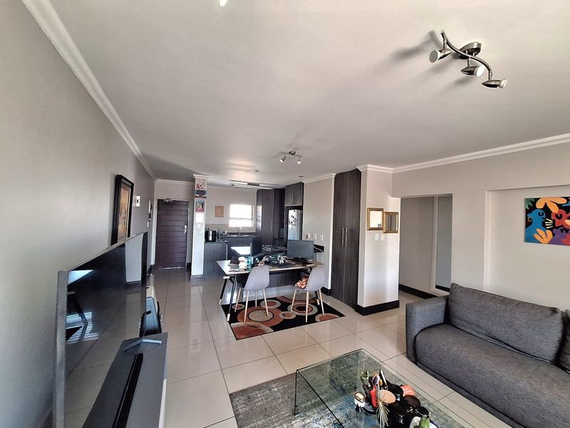 An open-plan living and kitchen area featuring tiled flooring, modern cabinetry, and recessed ceiling lighting, creating a functional and cohesive living space.