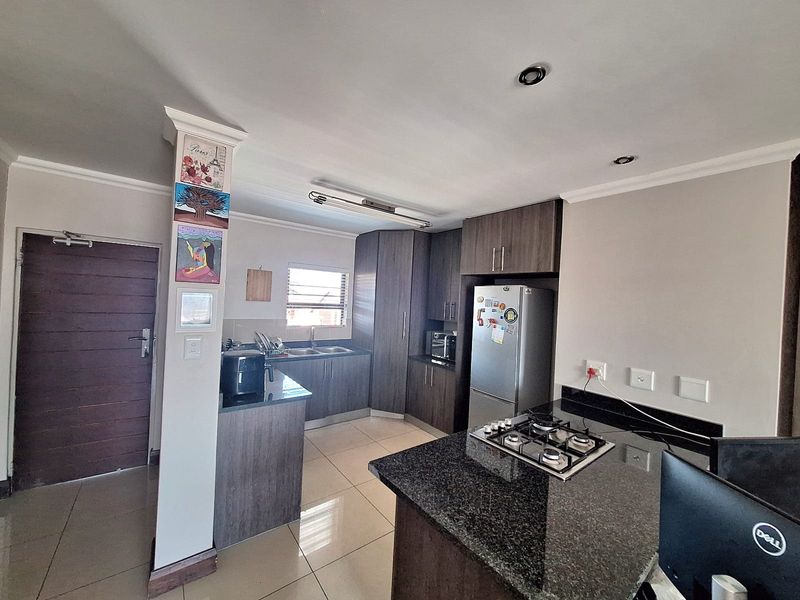 Modern kitchen featuring dark wood cabinetry, granite countertops, a gas hob, and tiled flooring, offering a functional and contemporary cooking space.