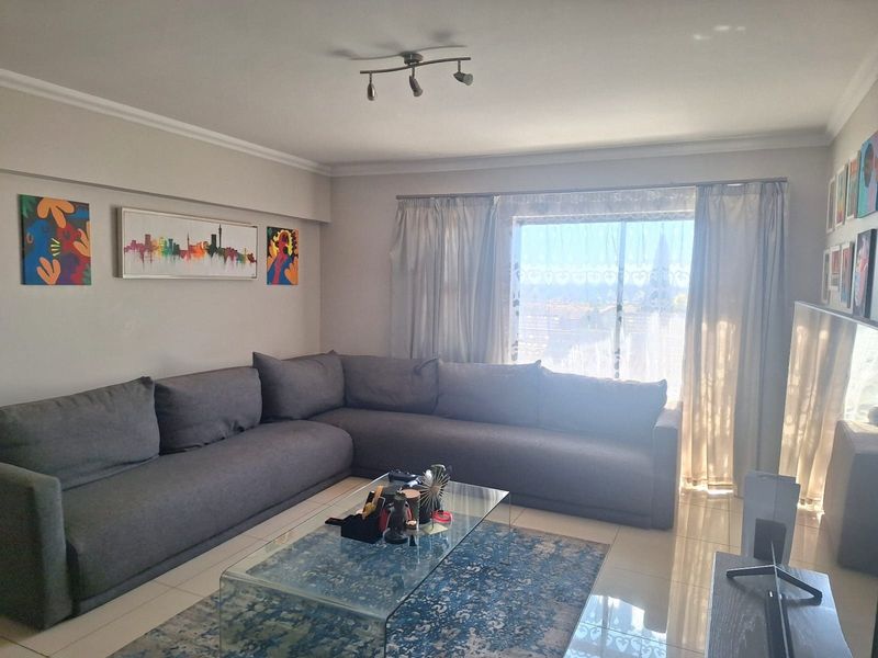 A well-maintained living room featuring tiled flooring, neutral walls, and a large window that provides ample natural light.