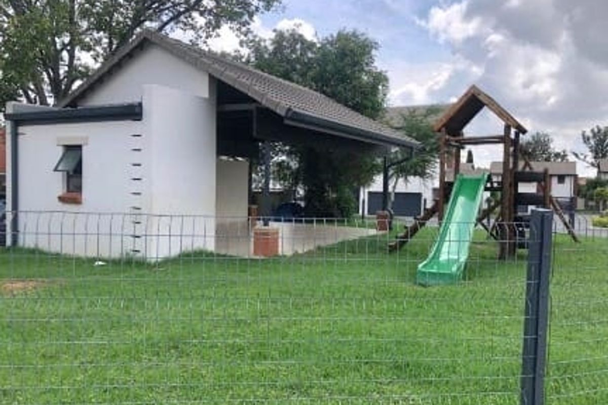 A communal outdoor area featuring a covered patio structure and a children's playground set within a fenced grassed yard.