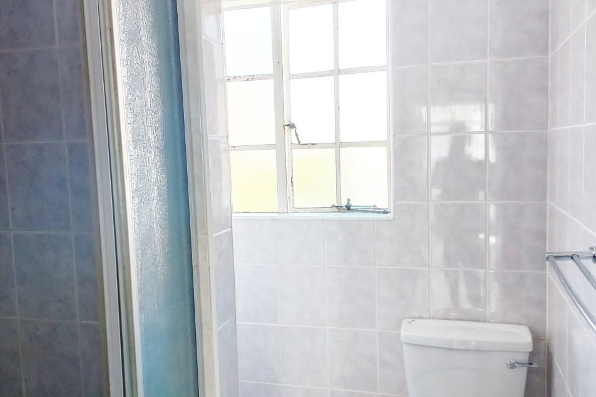 A functional bathroom featuring a shower enclosure, toilet, and neutral wall and floor tiling.
