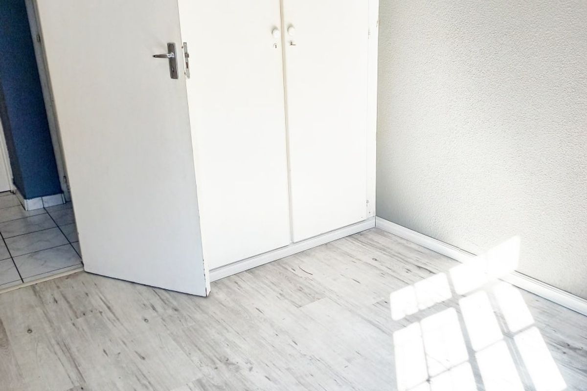 A bright, empty bedroom featuring light-toned laminate flooring and a built-in white wardrobe.
