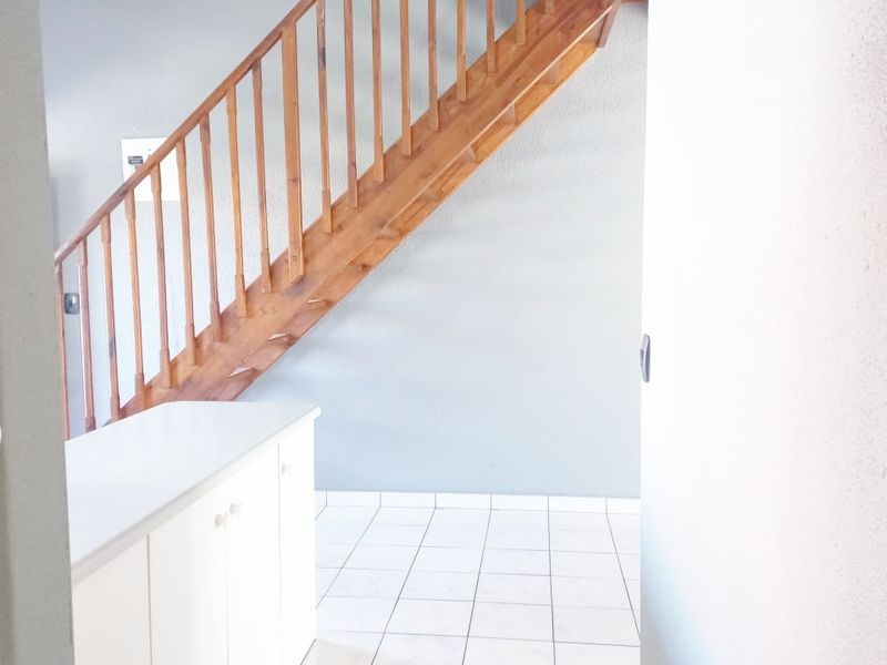 A bright hallway featuring a wooden staircase, tiled flooring, and built-in white cabinetry, offering a clean and functional transition space.