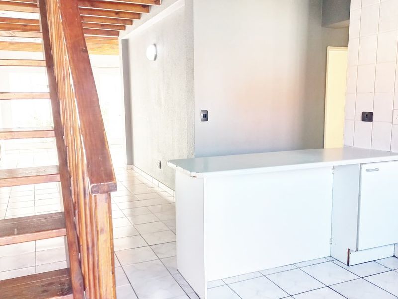 Open plan living area featuring a prominent wooden staircase, tiled flooring, and a built-in breakfast counter with tiled splashback.