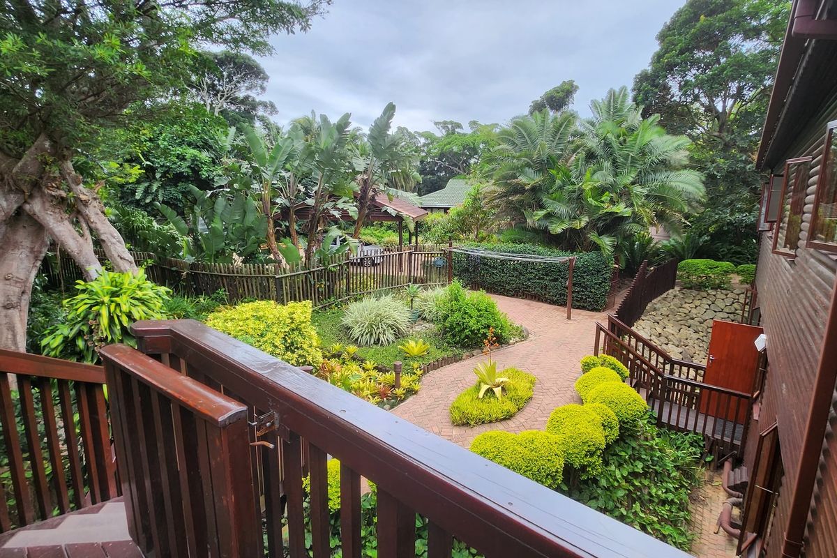 A view from an elevated timber deck overlooking a well-maintained rear garden with brick pathways, lush landscaping, and timber fencing.