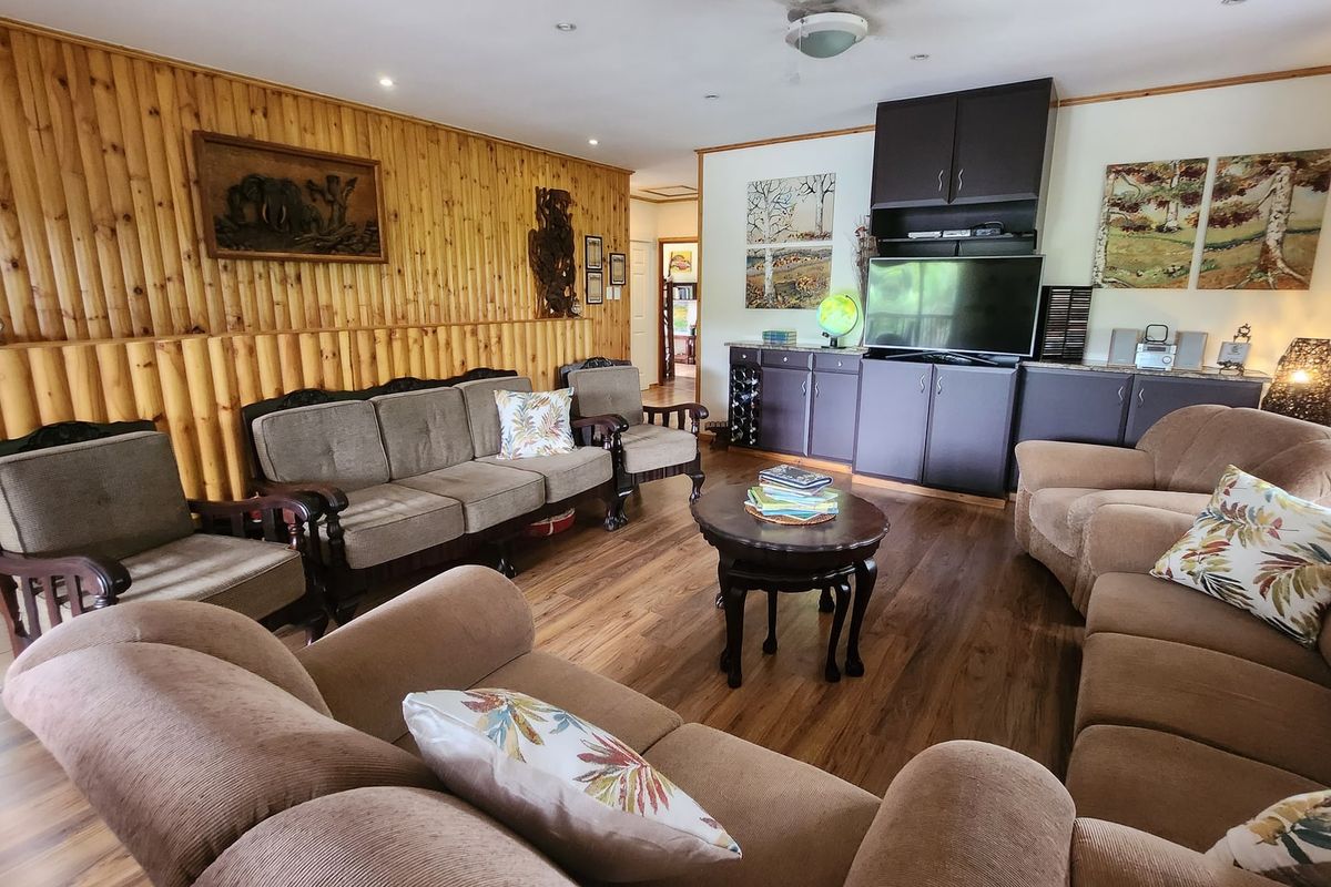 A living room featuring timber wall paneling, laminate flooring, recessed downlighting, and built-in cabinetry for storage and media display.